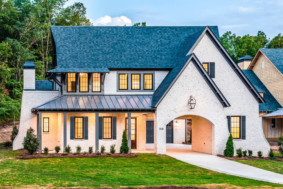 White brick home with an arched entry and illuminated windows at dusk.