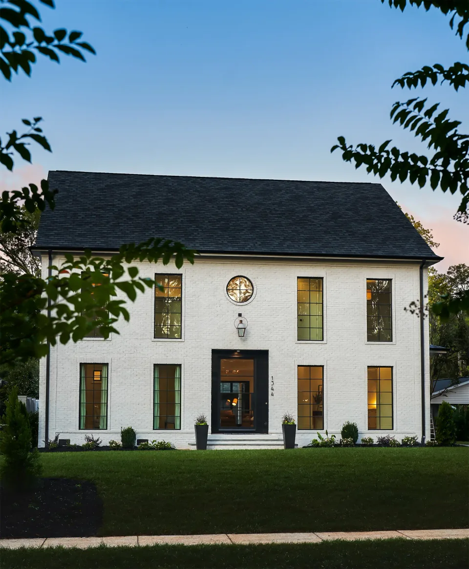 White brick home with tall windows and a dark front door, viewed from the lawn.