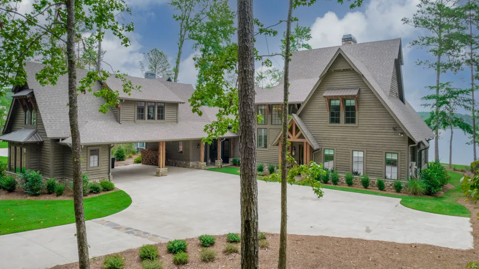 Lakeside home with a covered drive, stone piers and tall trees.