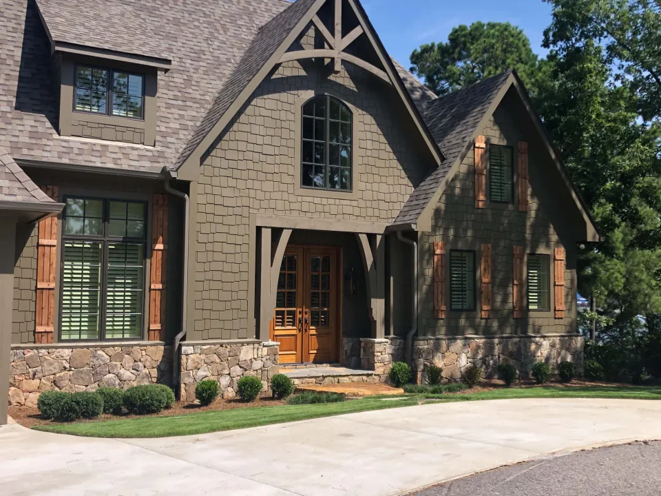 Shingled home with timber gables, wooden shutters and a stone base.
