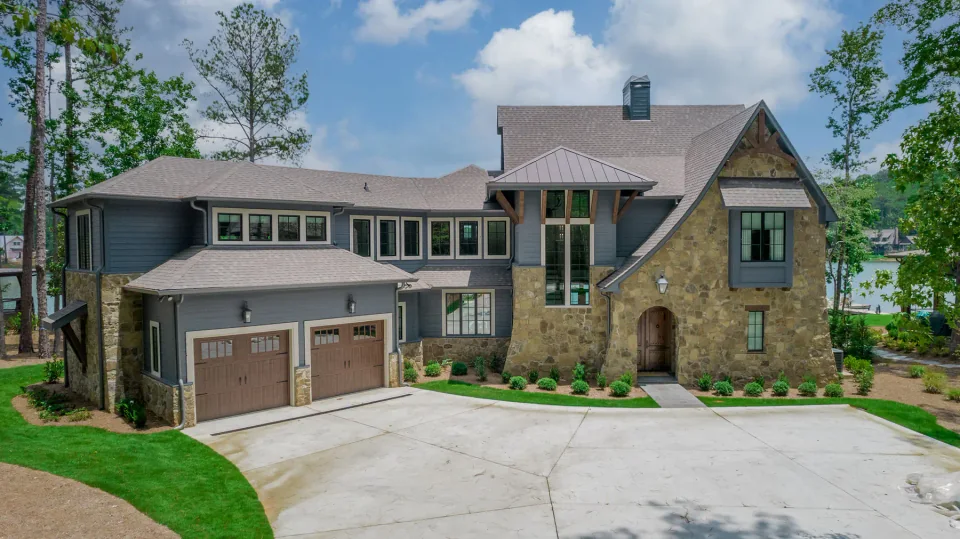 Stone and gray sided home with an arched entry and garage beside a lake.
