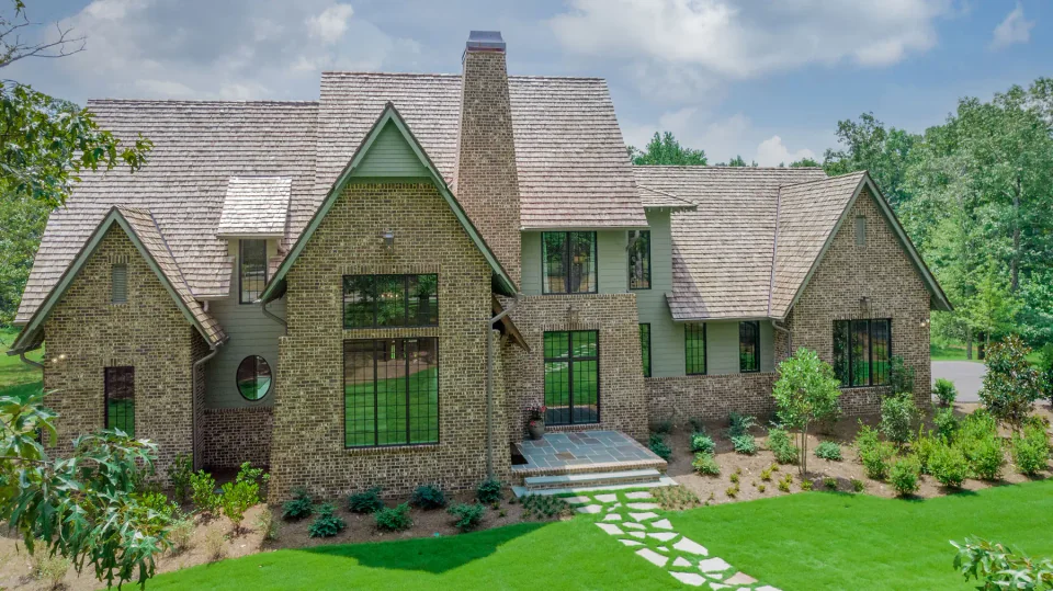 Brick home with tall dark windows, a central chimney and a stone path.