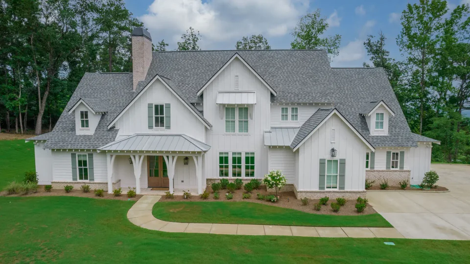 White home with green shutters, metal porch roofs and a curved front walk.