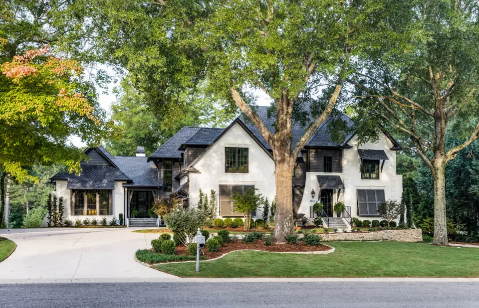 Renovated home with white walls, stone details and mature trees along the front drive.