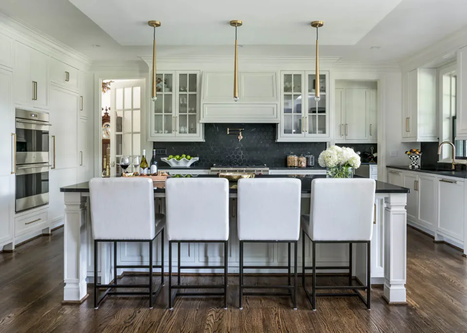 Kitchen with a large island, white cabinetry and dark pendant lights.